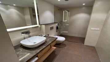 A modern bathroom with a large mirror, a vessel sink, a toilet, and a glass-enclosed shower.
