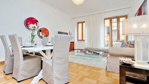 A modern living room with a dining area, featuring a white dining table, cushioned chairs, a glass coffee table, and a sofa. - 2 Apartments same building Piazza del Popolo 1+3 (Roma)