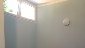 A single bed with a blue mattress and pillows, a bedside table with a lamp, and a window with a view of greenery. - Cozy apartment on the ground floor with a small terrace (Privlaka)