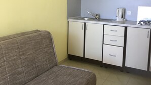 A compact kitchen with white cabinets, a grey sofa, and a small countertop. - Cozy apartment on the ground floor with a small terrace (Privlaka)