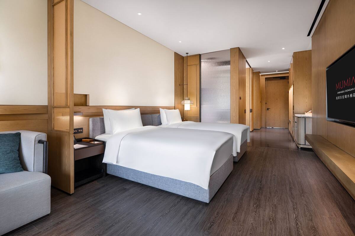 A modern hotel room with a large bed, a bedside table, a chair, and a TV screen.