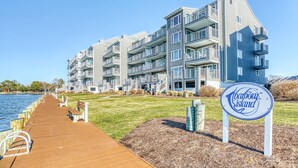Un ensemble d’appartements situé au bord de l’eau, avec une promenade en bois menant à la mer, une zone herbeuse et un panneau indiquant « Harbour Island ».