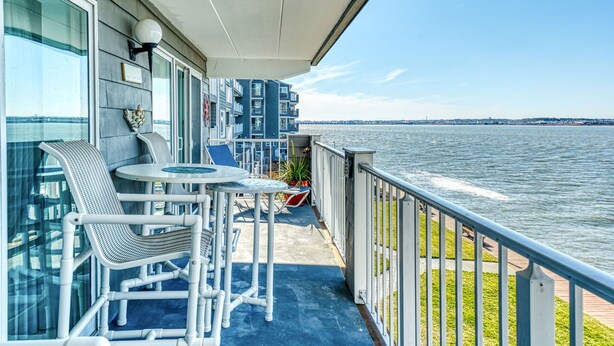 Un balcon avec une table et des chaises, donnant sur une étendue d’eau où l’on aperçoit un pont au loin.
