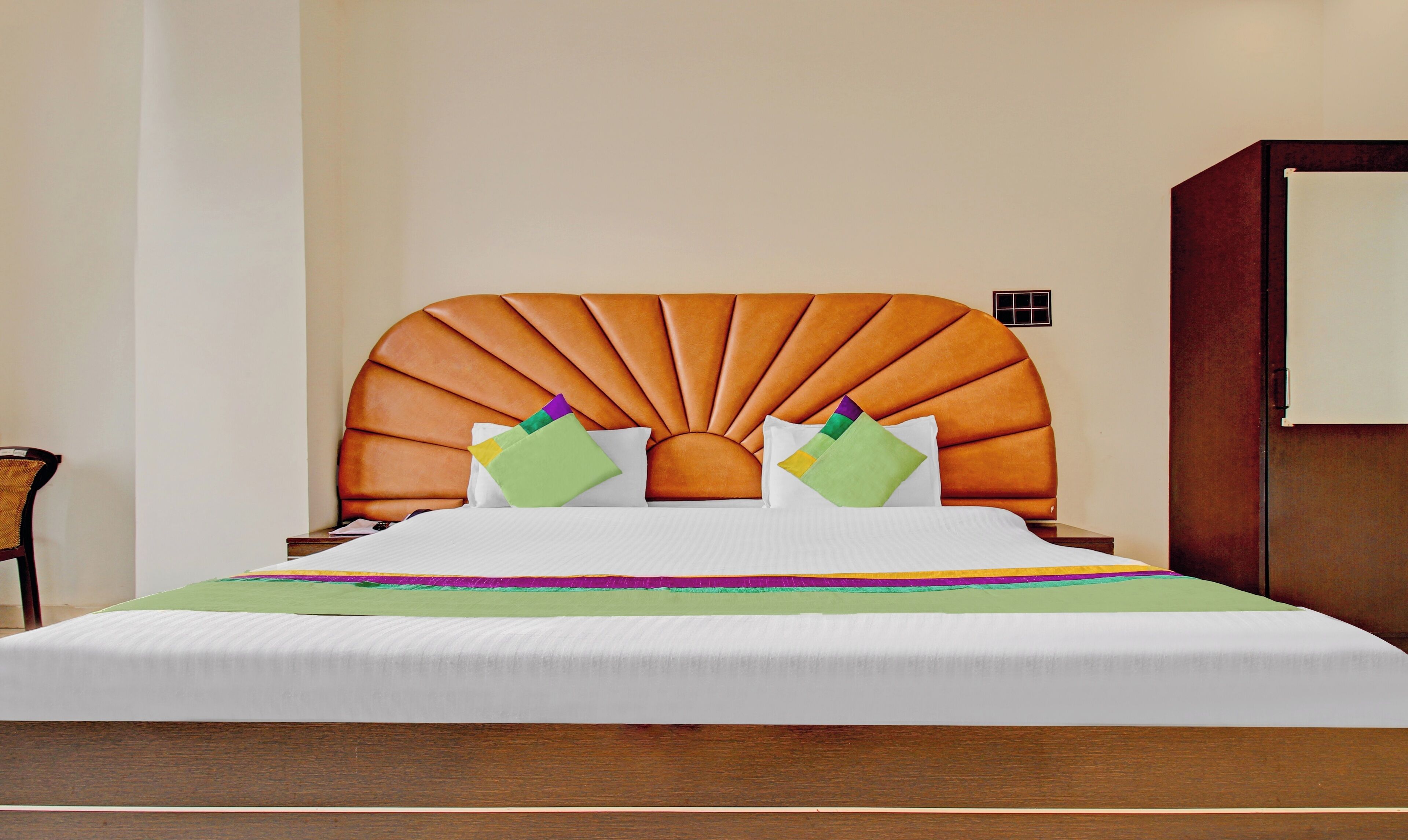 A bed with a unique orange headboard, white bedding, and colorful pillows.