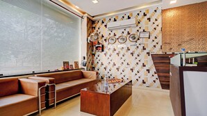 Un área de recepción moderna con un sofá de cuero marrón, una mesa de centro de madera y una pared con un diseño que incluye relojes y señales que indican Nueva York, India y Londres.