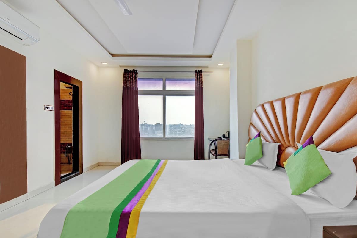 A hotel room with a large bed, a view of the city through the window, and a door to the bathroom.