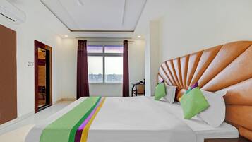 A hotel room with a large bed, a view of the city through the window, and a door to the bathroom.