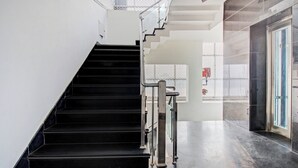 Una escalera moderna con peldaños negros y barandillas de metal, que conduce a una puerta de cristal.