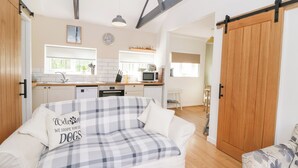 A cozy living room with a plaid sofa, a kitchen in the background, and a wooden door. - Dinefwr Cottage (Carmarthen)