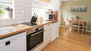 A modern kitchen with white cabinets, a Bosch oven, a microwave, and a dining area with a wooden table and chairs. - Dinefwr Cottage (Carmarthen)