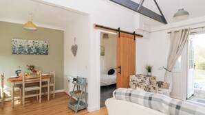 A cozy living room with a wooden floor, a sofa, a dining table with chairs, a kitchen area with a sink and a hanging light fixture. - Dinefwr Cottage (Carmarthen)