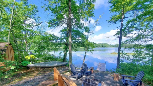 A lakeside campsite with a wooden deck, chairs, and a canoe.