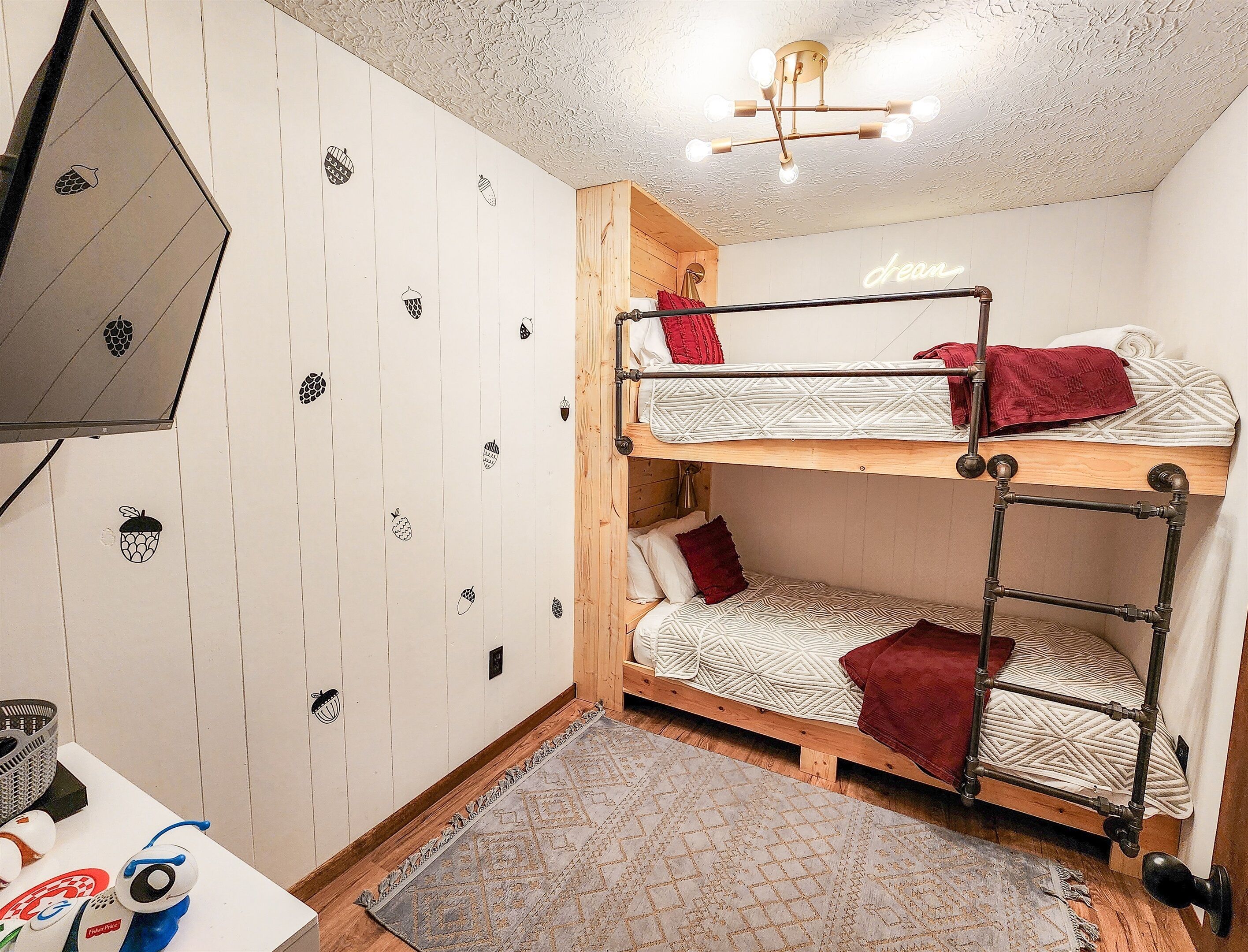 Een slaapkamer met stapelbed, een houten hoofdbord, een kamerkleed met dessin en een plafondlamp.