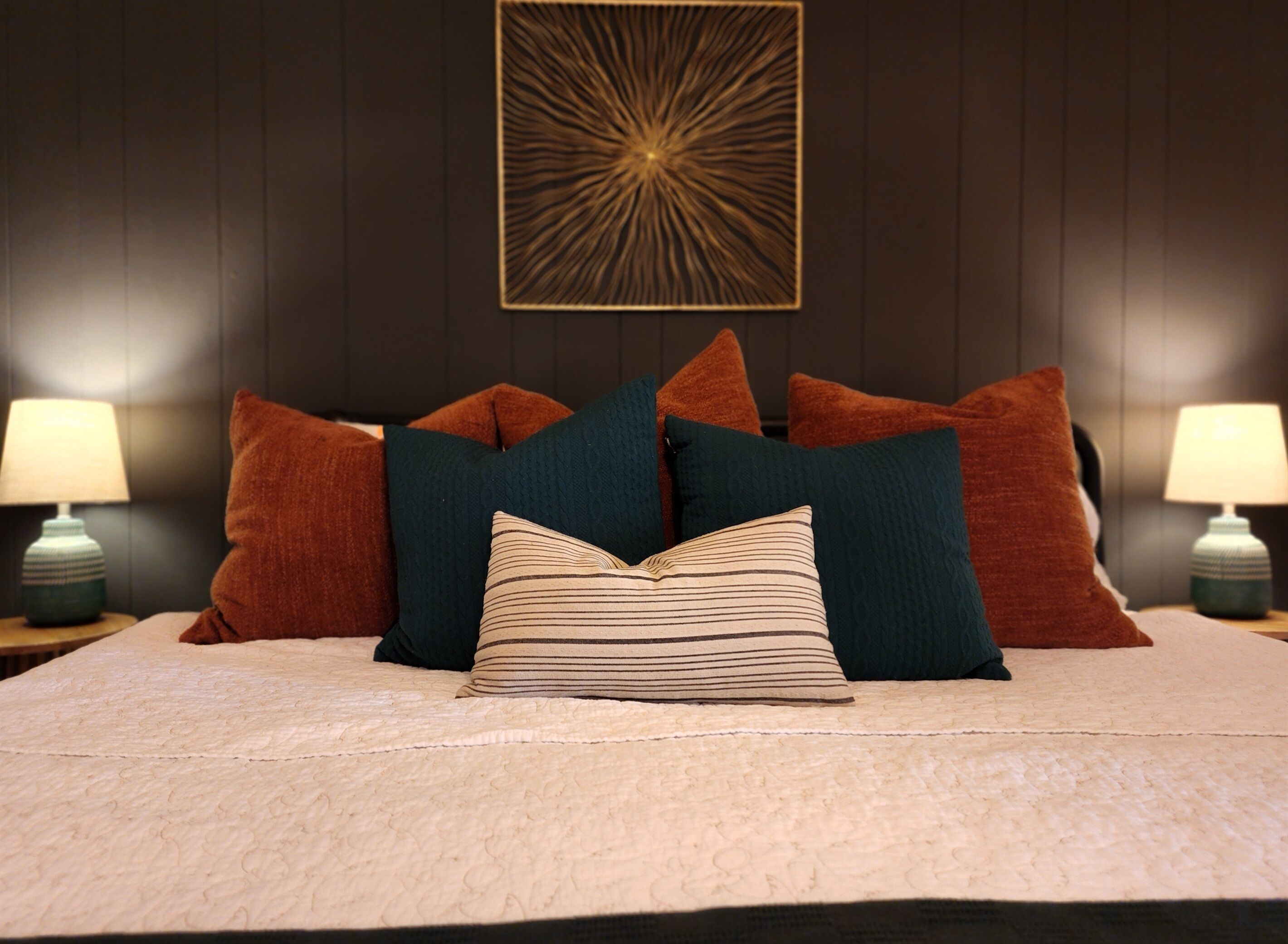 A neatly made bed with multiple pillows and a decorative wall piece above it.