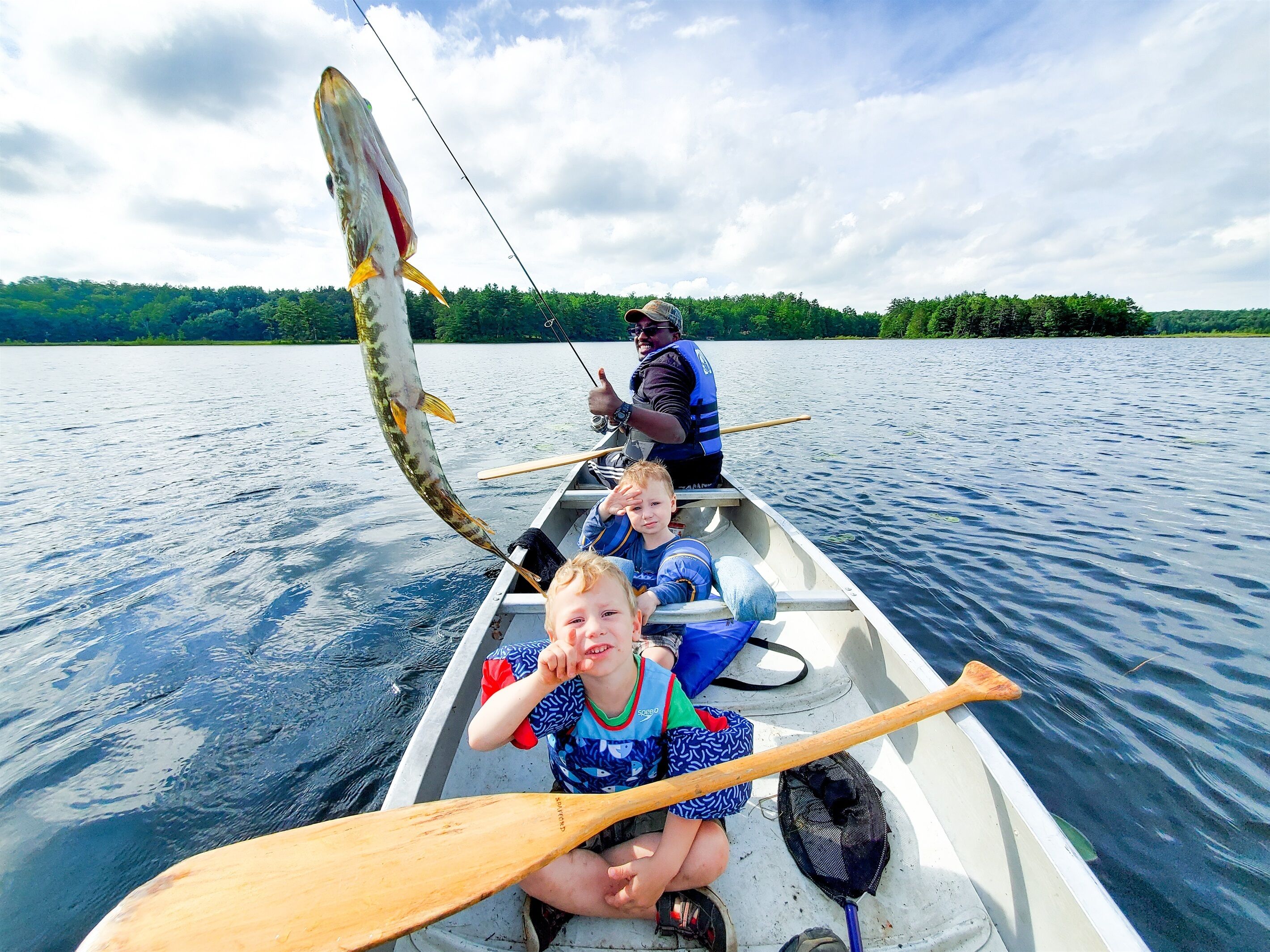 En båt med två personer och ett barn, där en av dem håller i en fiskespö.