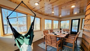 A wooden interior with a dining table set for six, surrounded by chairs, and a hammock hanging from the ceiling.