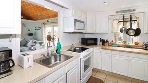 A kitchen with white cabinets, a microwave, a stove, a sink, and a window with a view of the beach. - An Unfettered View | Wheelchair Accessible Oyster Bay Waterfront Ranch w/ Long Pier for Crabbing (Chincoteague Island)