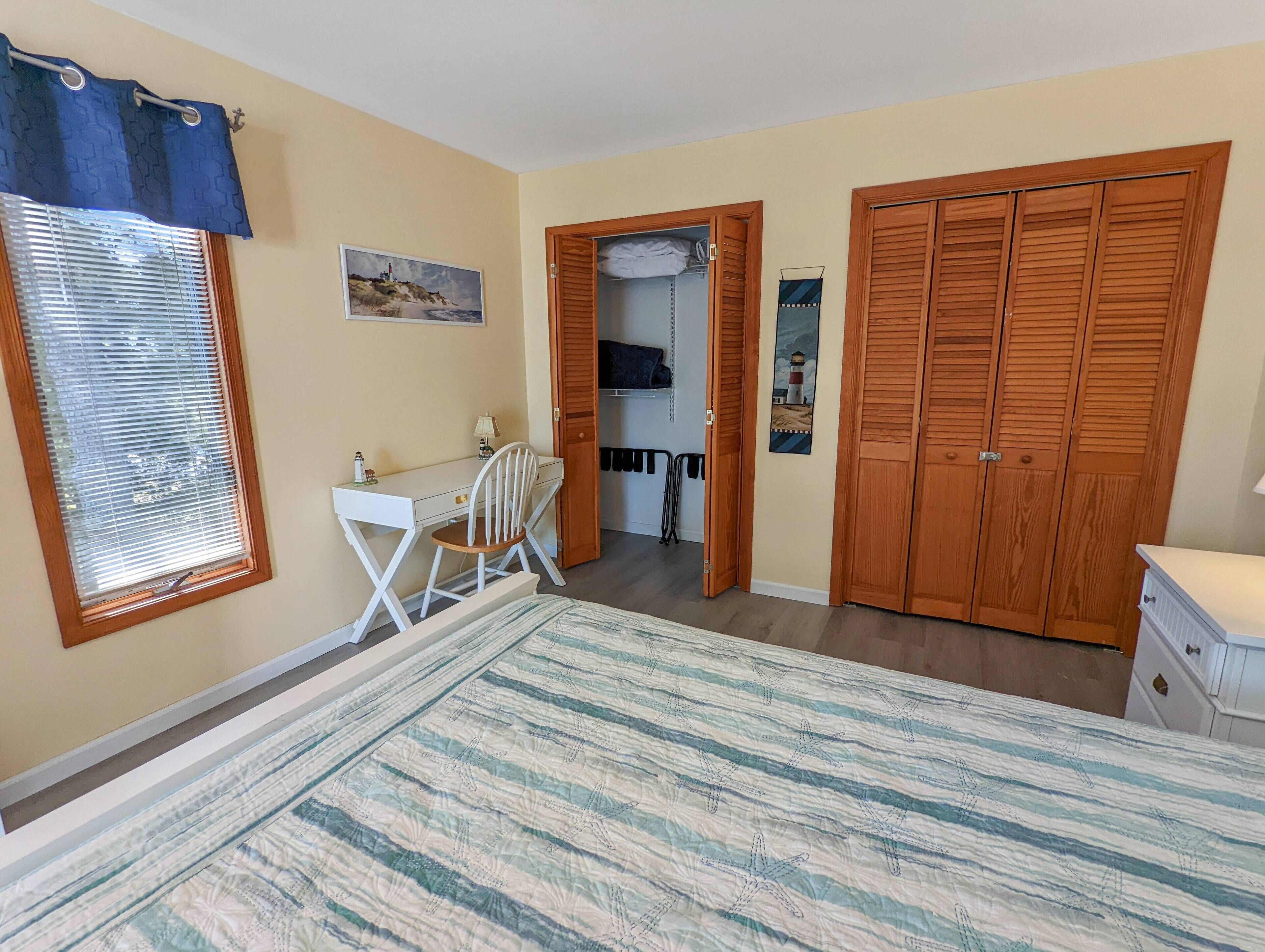 Een slaapkamer met een bed, een bureau, een stoel, een kledingkast en een raam met zonwering.