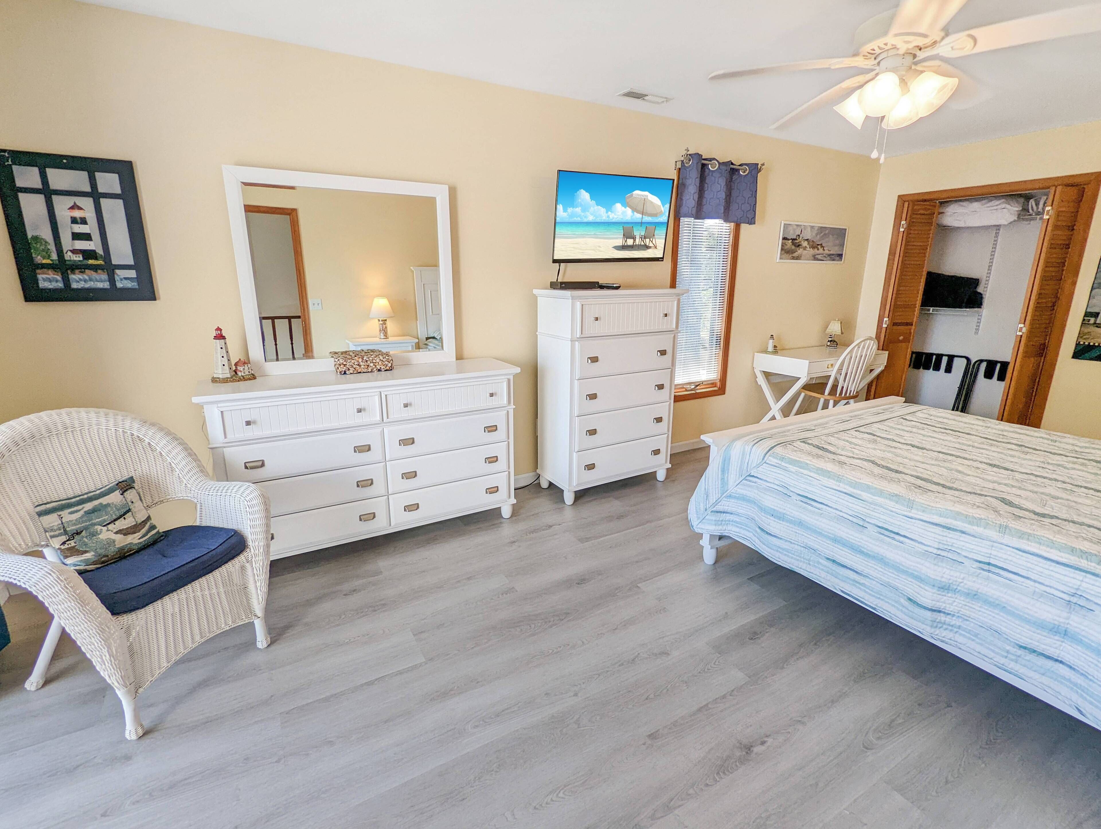 Een slaapkamer met een bed, een dressoir, een stoel, een bureau en een plafondventilator.