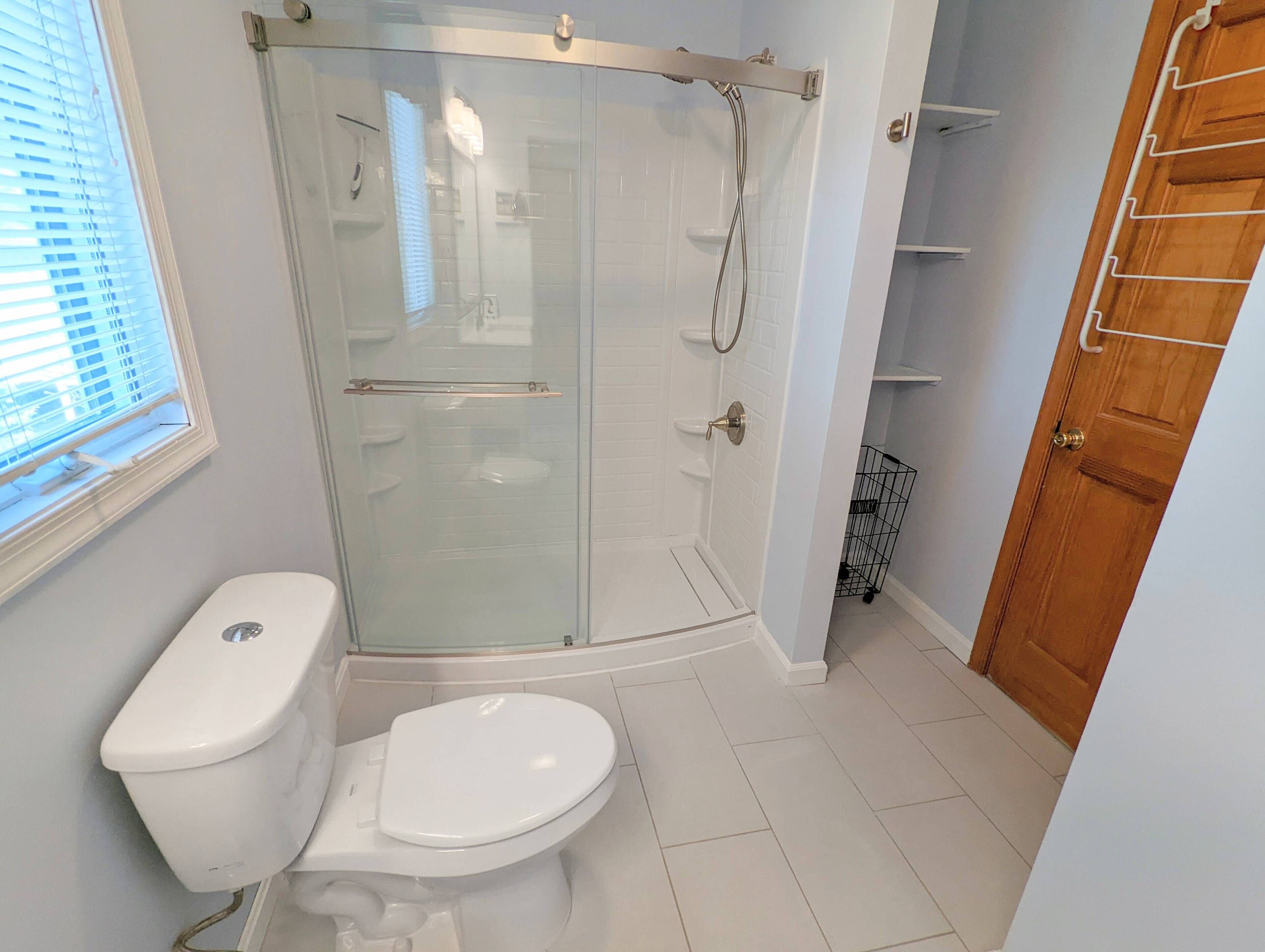 A bathroom with a glass-enclosed shower, a toilet, and a wooden door.