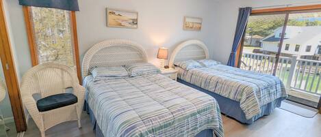 A bedroom with two beds, a chair, a ceiling fan, and a window with a view of a house.