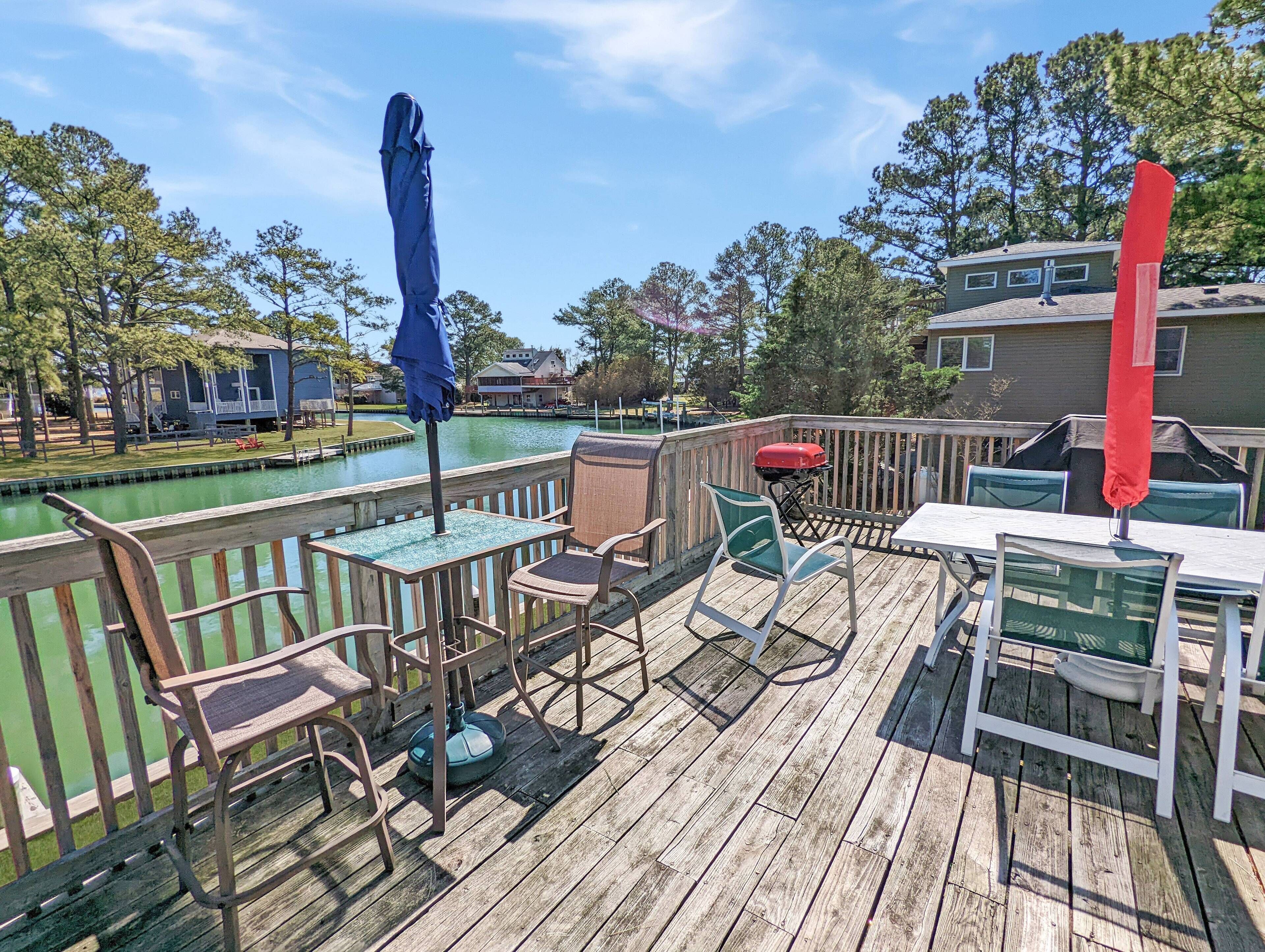 A wooden deck with outdoor seating, a barbecue grill, and a view of a body of water.