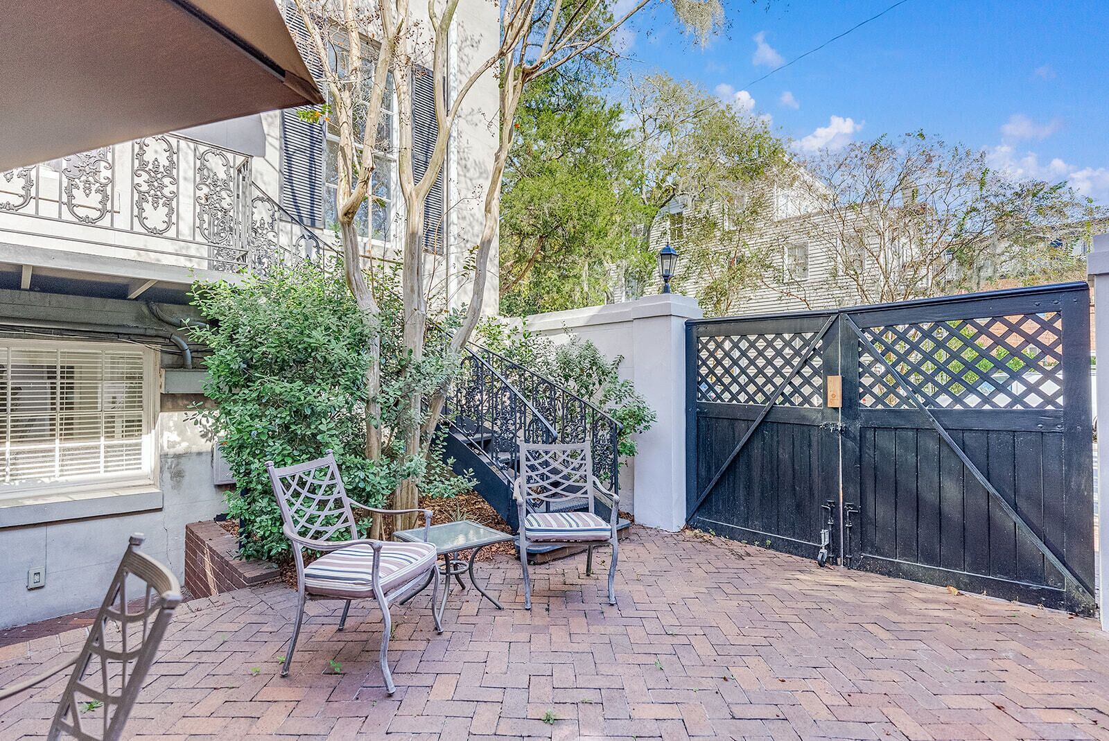 A patio with two metal chairs and a table, a black gate, and a white building with a window and a balcony.