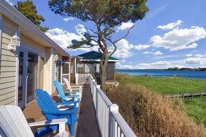A wooden deck with blue chairs, a covered seating area, and a view of the water. - Heron's Cove on Salt Meadow | Bayfront Views, Dock, King Suites, Fireplace + Pet Friendly (Chincoteague Island)