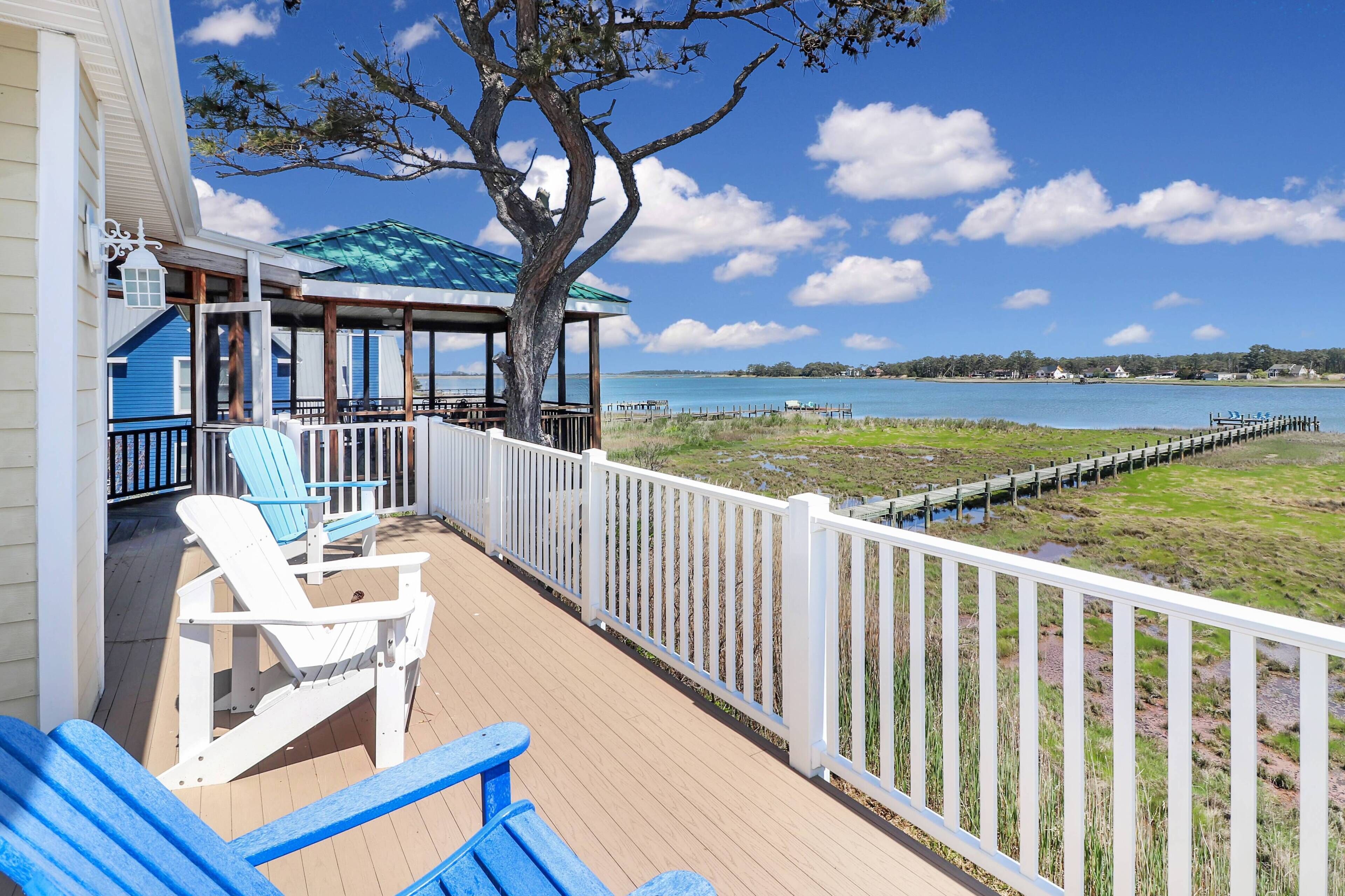 A wooden deck with two blue Adirondack chairs, a covered area with a blue roof, and a view of a body of water.