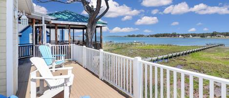 A wooden deck with two blue Adirondack chairs, a covered area with a blue roof, and a view of a body of water.