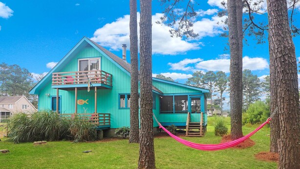 Una casa turchese con un balcone, immersa nel verde e con un'amaca.