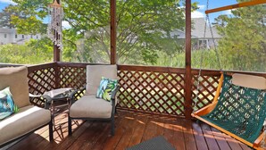 A wooden deck with a hammock, a cushioned chair, and a small table. - Seas the Day | Bright Duplex + Screened Porch + Community Pool + Kid Bunk Room (Chincoteague Island)