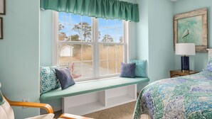 A room with a window seat, a bed, a lamp, and a painting on the wall. - Seas the Day | Bright Duplex + Screened Porch + Community Pool + Kid Bunk Room (Chincoteague Island)