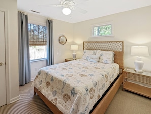 Quarto com uma cama, duas luminárias de cabeceira, um ventilador de teto, uma janela com persianas e um pequeno janelão sobre a cama.