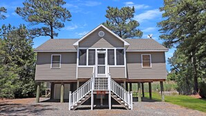 A two-story house with a central staircase and a porch. - Serenity at Oyster Bay | Screened Porch, Preserve Views + Near Water Access, Firepit (Chincoteague Island)