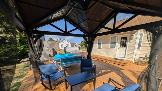 A covered outdoor deck with a wooden floor, blue cushioned seating, and a barbecue grill. - Shell Cottage | East Side Assateague Channel Views w/ Decks, Outdoor Shower, Boat Parking & Pets (Chincoteague Island)