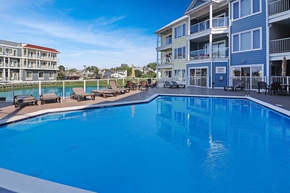 A swimming pool with lounge chairs and a deck area, surrounded by multi-story buildings with balconies.