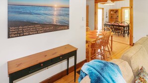 Une pièce comprenant une table à manger en bois, des chaises, un banc et un canapé. Une fenêtre offre une vue sur l’océan.