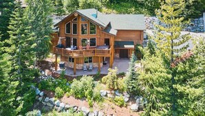A large wooden lodge with a balcony, surrounded by trees and a stone wall.