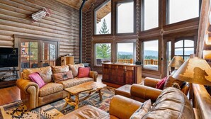 A log cabin interior with a large window, a sofa, a coffee table, and a television.