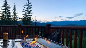 A fire pit with burning wood, a can of beer, and a view of mountains and trees.