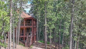 A two-story wooden cabin with a balcony, surrounded by dense pine trees. - Gold Baron Lodge (Lead)