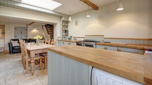 Una cocina amplia con encimeras de madera, un comedor con mesa y sillas, y una escalera visible que lleva a otro nivel.