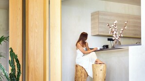 Un interno moderno con una donna seduta su uno sgabello di legno a un bancone della cucina, un divano con cuscini decorati e una pianta di cactus.