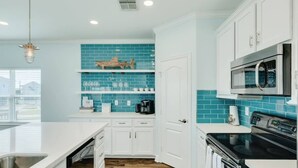 A kitchen with white cabinets, a blue tiled backsplash, a stainless steel sink, and a black stove. - Lollygaggin by the Beach! Fenced Yard, Outdoor Bar! (Galveston)