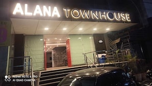 The exterior of Alana Townhouse with a prominent illuminated sign, a staircase leading to the entrance, and a parked car in front.