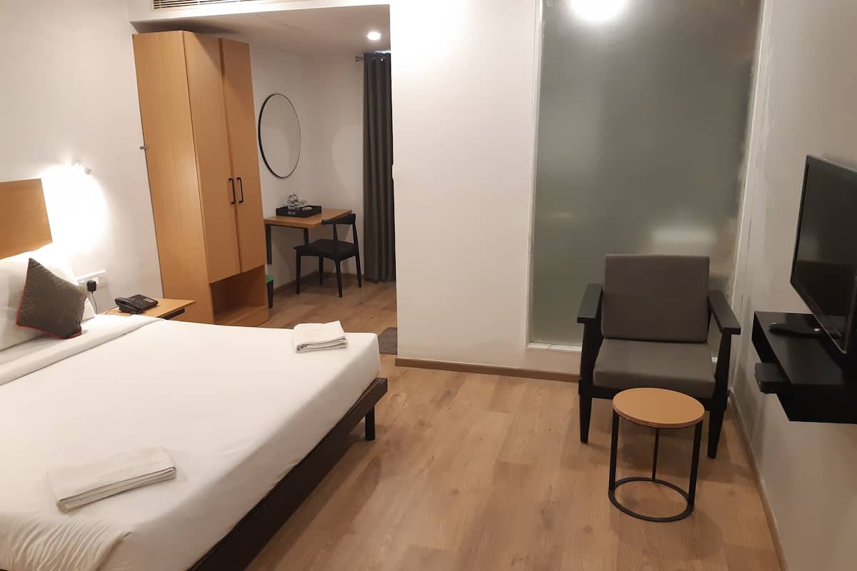 Ein Hotelzimmer mit Bett, Schreibtisch, Sessel, Fernseher und Spiegel.