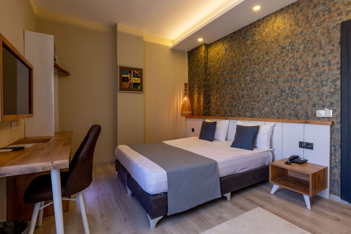 A modern bedroom with a large bed, bedside table, and a desk with a chair.