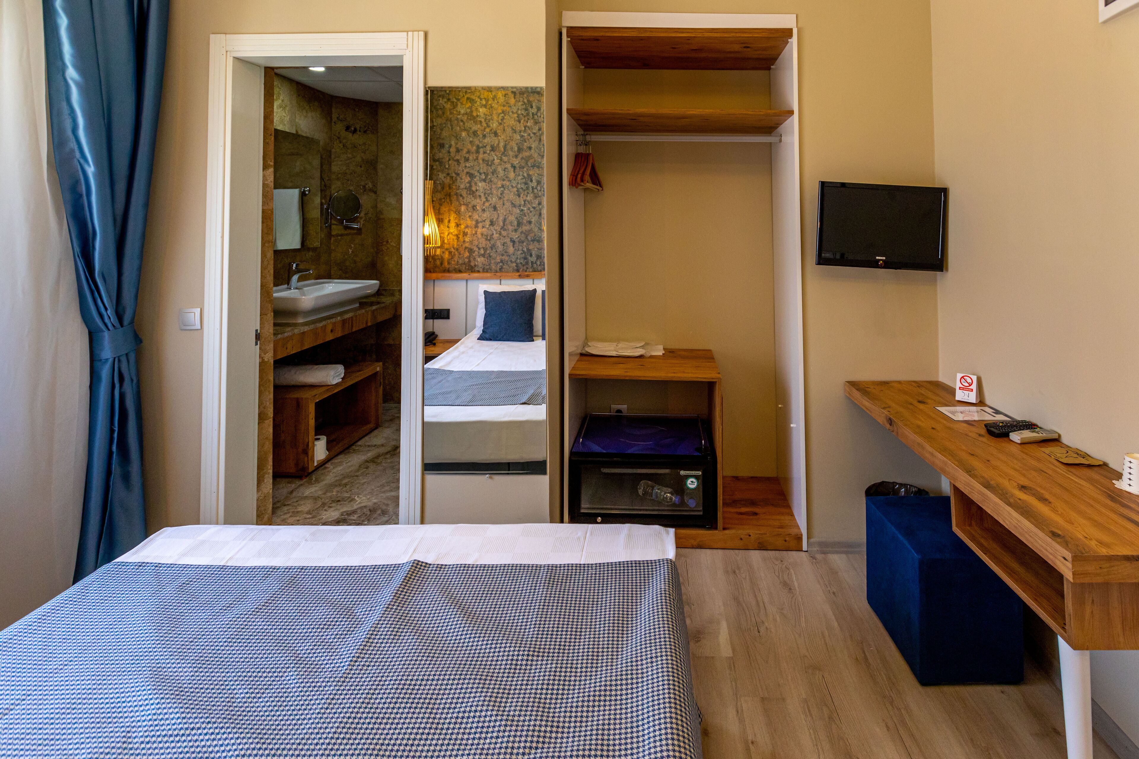 A bedroom with a bed, a wooden desk, a TV, and a bathroom visible through an open door.