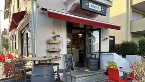 An outdoor seating area with tables and chairs, a large barrel, and a chalkboard menu outside a café.